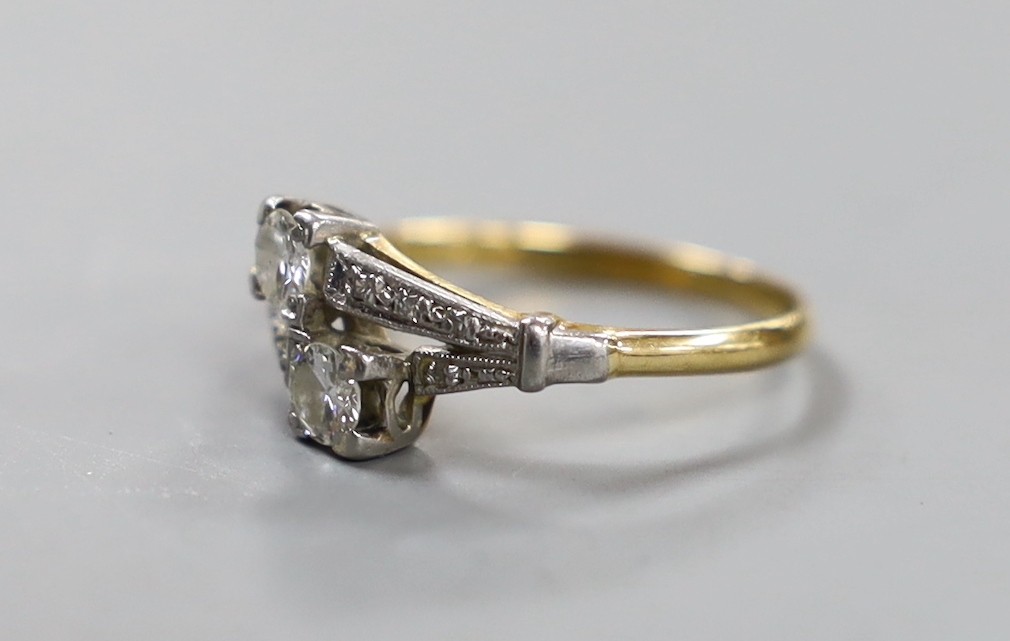 An 18ct, plat and two stone diamond crossover ring, with diamond set shoulders, size N/O, gross weight 2.7 grams.